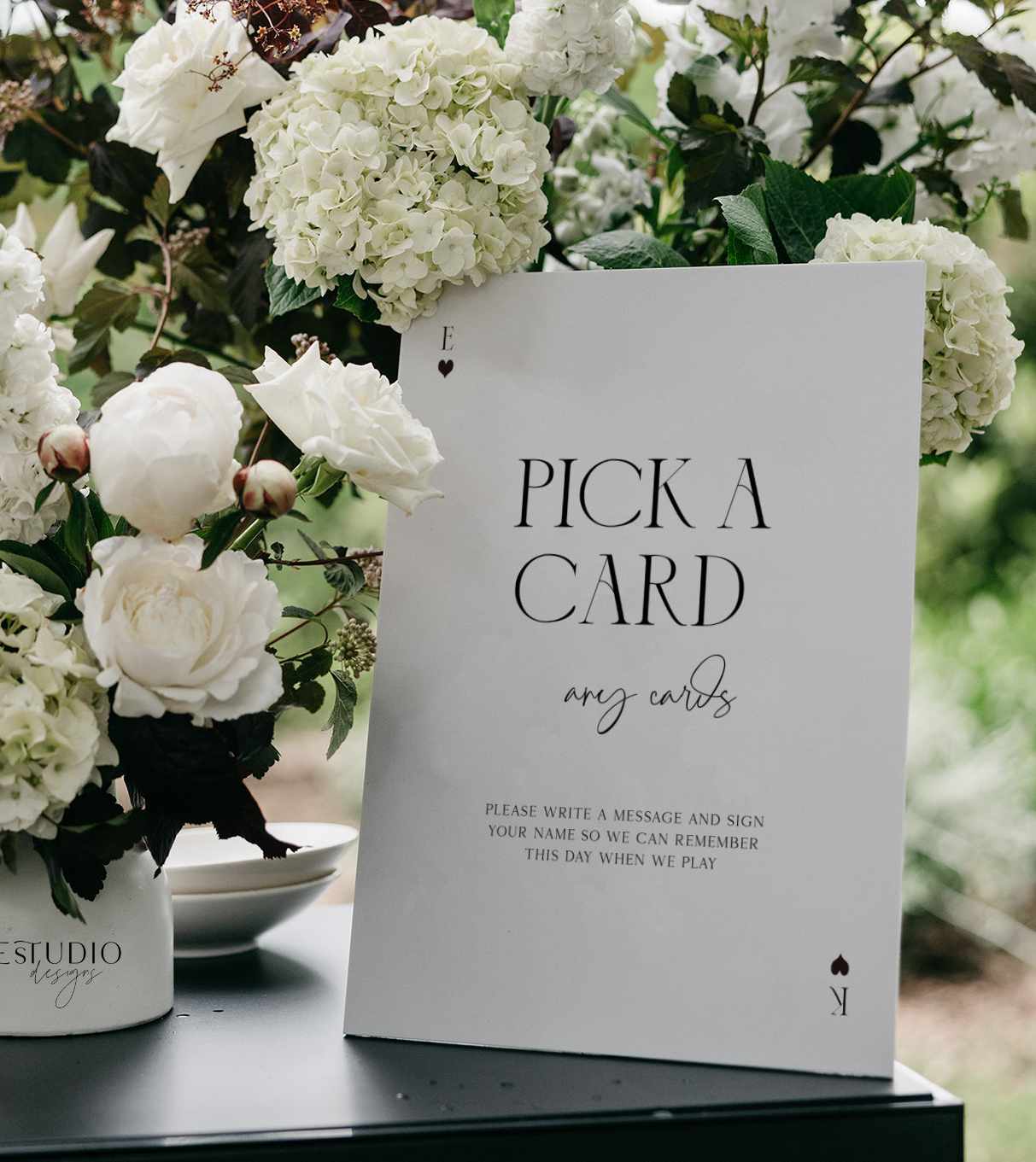 Modern Playing Card Guest Book sign with 'Pick a Card' text on a table with white flowers in the background