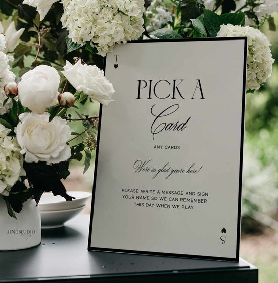 wedding table sign with text Pick A Card in black and off-white background sign next to white flowers vase