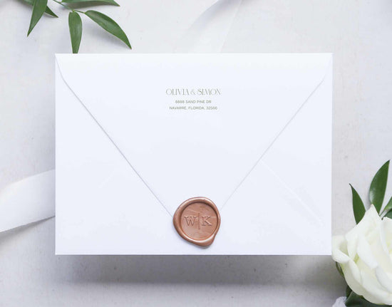 White envelope with return address on back flap and a wax seal and floral arrangement on a light background