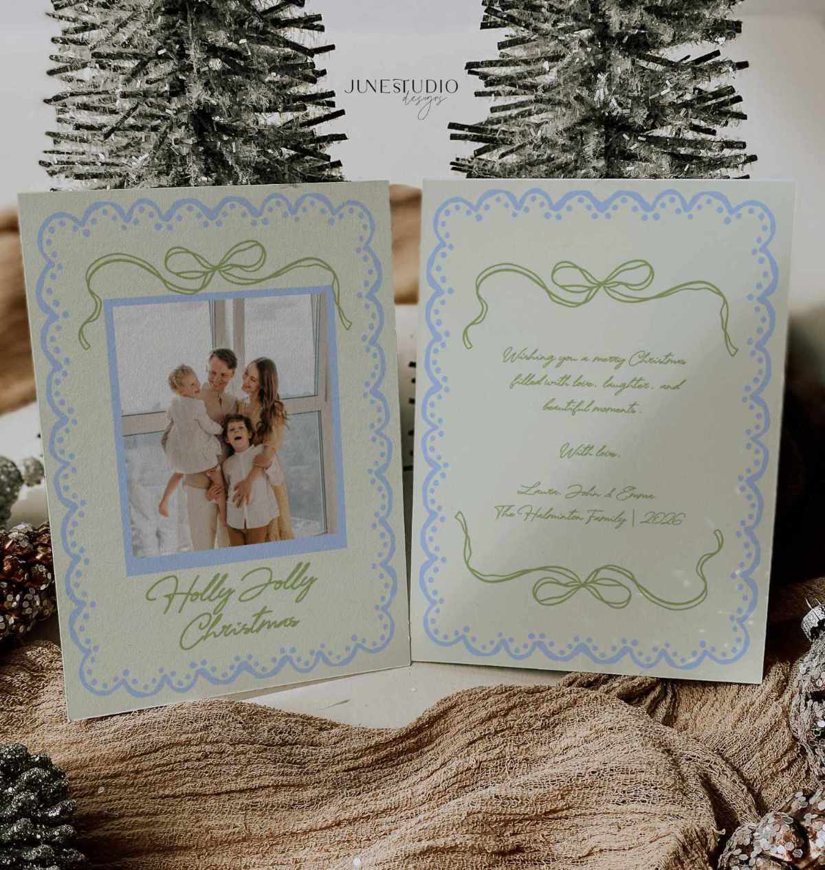 A double-sided Christmas greeting card set displayed open, showing a photo of a family on the front and elegant script text on the back. The card has a pale green and blue scalloped border with bow motifs.